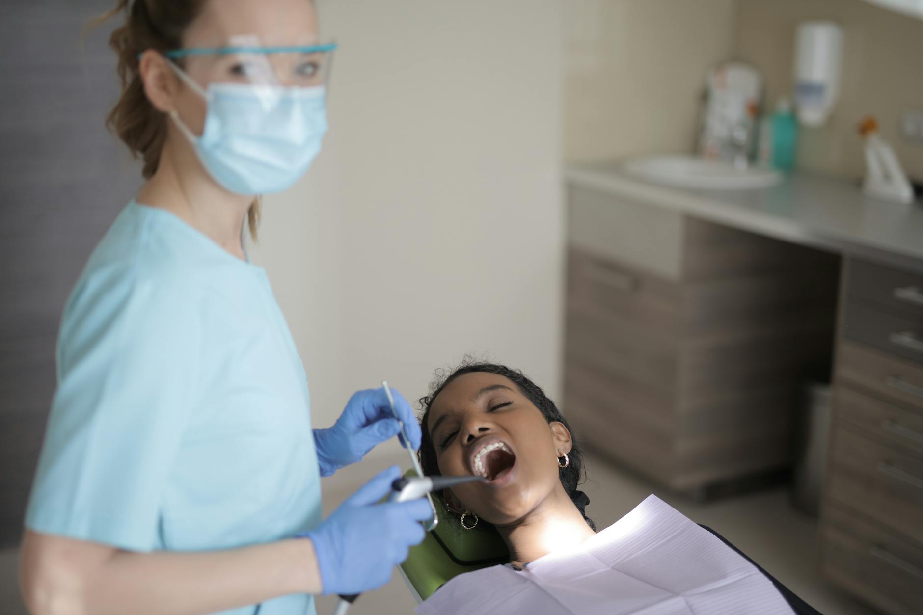 Dentysta w środkach ochrony osobistej bada zęby pacjenta w gabinecie