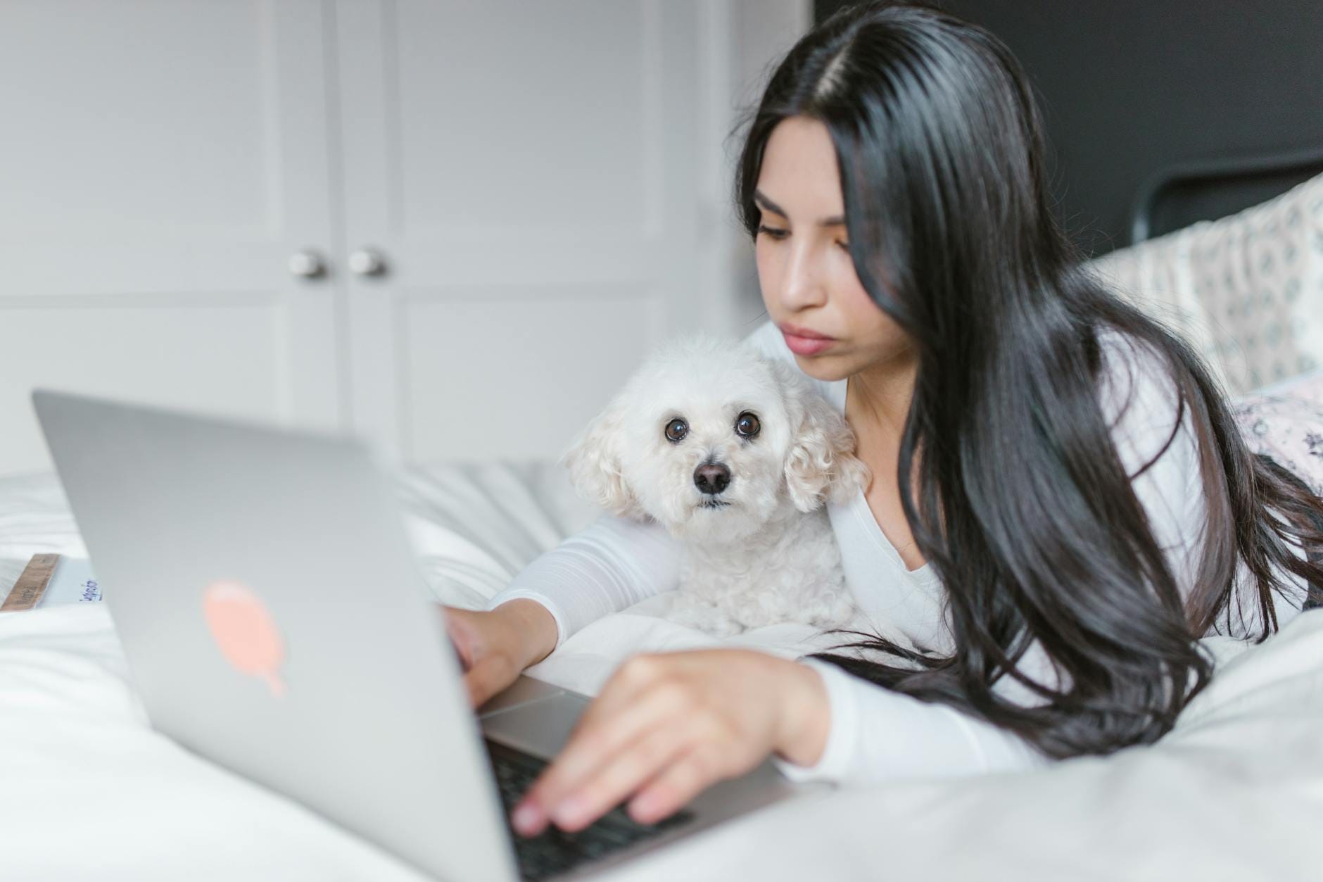 Kobieta pracuje na laptopie w domu, a obok niej spokojnie leży pies