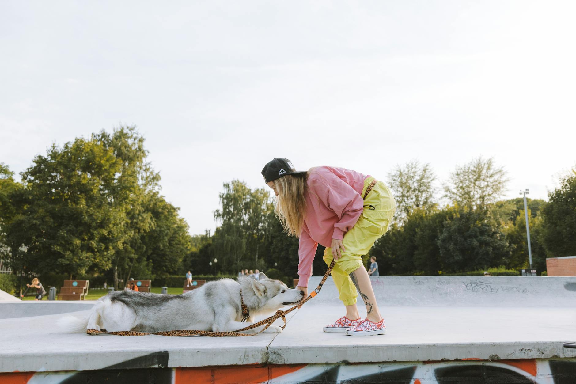 Kobieta bawi się z psem husky w miejskim skateparku wśród drzew